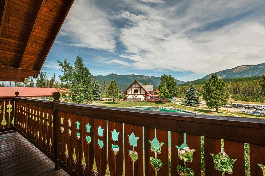 ID: A photo of the view from a deck ,with trees, mountains and a cabin in the distance. End ID.